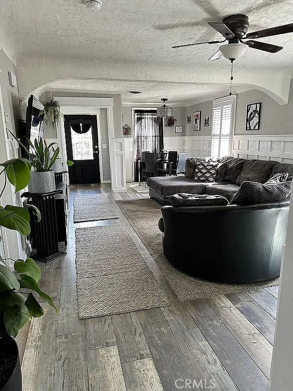 living area with a ceiling fan, a wainscoted wall, a textured ceiling, and hardwood / wood-style flooring