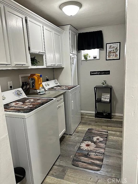 washroom with cabinet space, washer and dryer, dark wood-type flooring, and baseboards