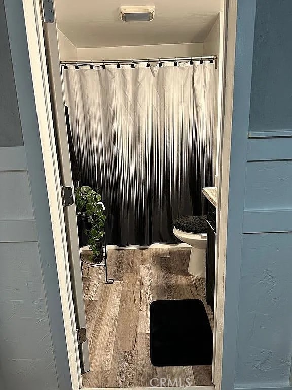 full bath featuring wood finished floors, toilet, and a shower with curtain