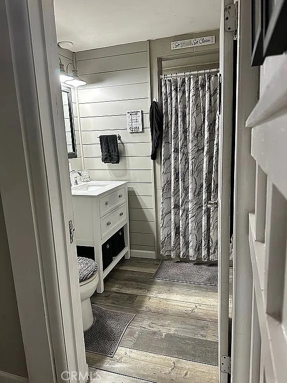 bathroom with wood finished floors, vanity, toilet, and curtained shower