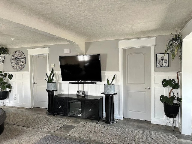 living area featuring a decorative wall, a textured ceiling, a wainscoted wall, and wood finished floors