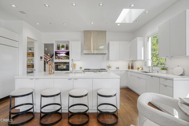 1116 Linda Flora Dr, Los Angeles, CA 90049 - kitchen featuring wall chimney exhaust hood, a sink, a skylight, dark wood-style floors, and a kitchen bar