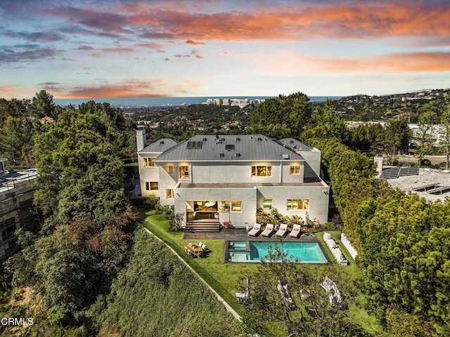 1116 Linda Flora Dr, Los Angeles, CA 90049 - back of house at dusk with a balcony, stucco siding, an outdoor pool, a patio area, and a fenced backyard