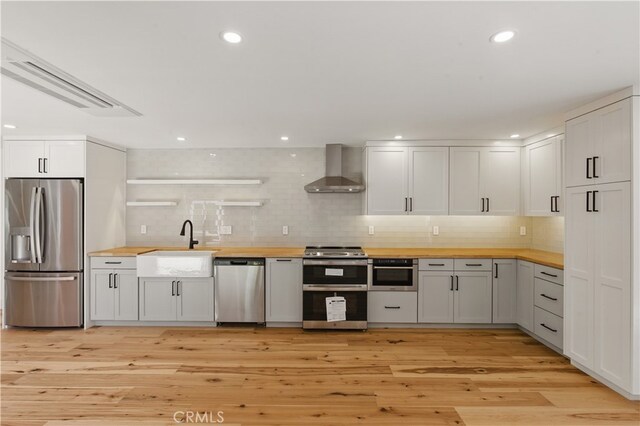 kitchen with stainless steel appliances, wooden counters, wall chimney exhaust hood, open shelves, and recessed lighting