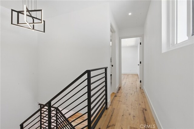 hall with an upstairs landing, light wood finished floors, recessed lighting, and baseboards