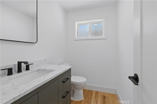 half bath featuring toilet, wood finished floors, vanity, and baseboards