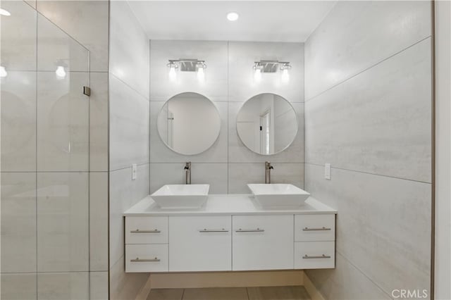 full bathroom featuring tile walls, a tile shower, double vanity, and tile patterned flooring