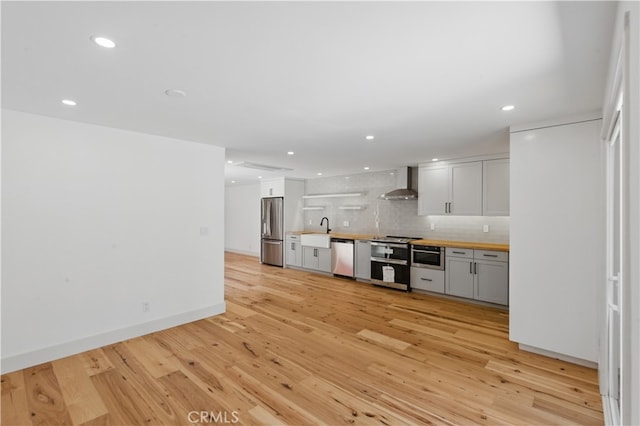 kitchen with appliances with stainless steel finishes, wall chimney range hood, butcher block counters, light wood-style floors, and recessed lighting