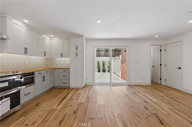 kitchen with butcher block countertops, light wood-style flooring, tasteful backsplash, stainless steel oven, and wall oven