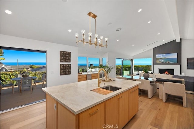 23262 Ellice Cir, Dana Point, CA 92629 - kitchen with light wood-style flooring, decorative light fixtures, a fireplace, an island with sink, and light brown cabinetry