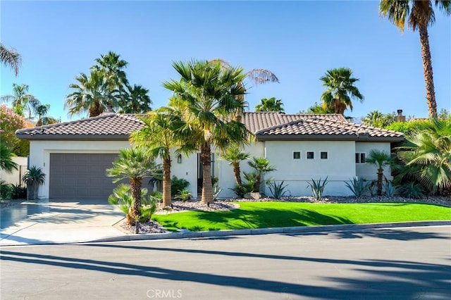 mediterranean / spanish house with stucco siding, concrete driveway, an attached garage, a tiled roof, and a front yard