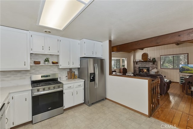 1027 Nesthorn Dr, Crestline, CA 92325 - kitchen featuring stainless steel appliances, light countertops, white cabinets, a brick fireplace, and beamed ceiling