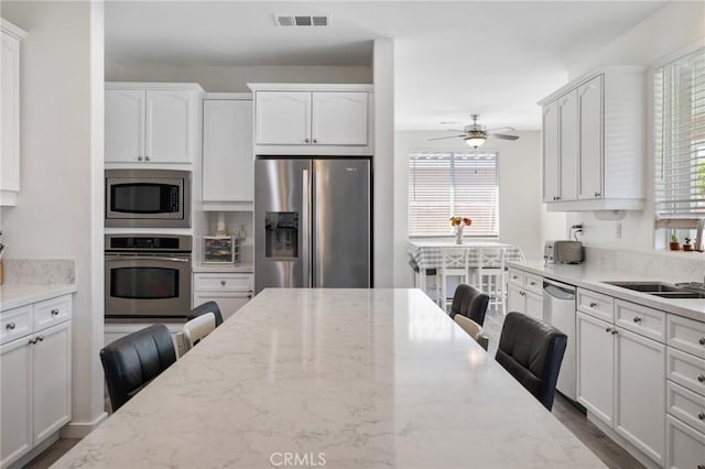 kitchen with stainless steel appliances, white cabinets, ceiling fan, and light stone countertops