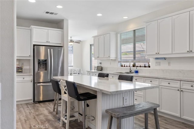 kitchen with stainless steel fridge with ice dispenser, light wood finished floors, a sink, white cabinets, and recessed lighting