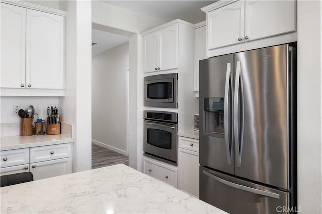 kitchen with stainless steel appliances, white cabinetry, light stone countertops, and baseboards
