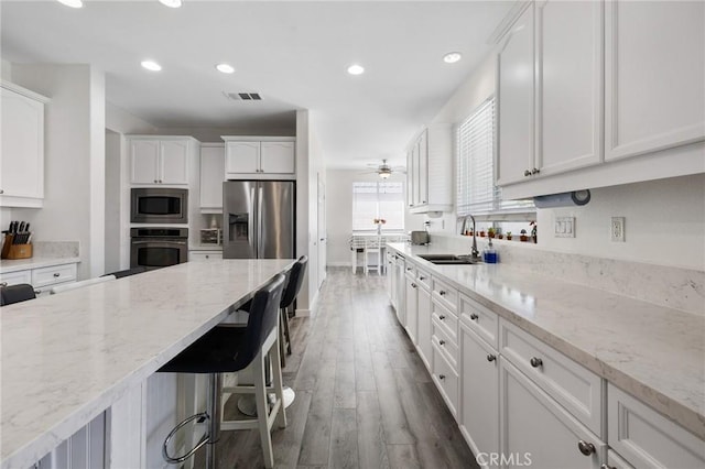 kitchen with a sink, appliances with stainless steel finishes, white cabinetry, wood finished floors, and a breakfast bar