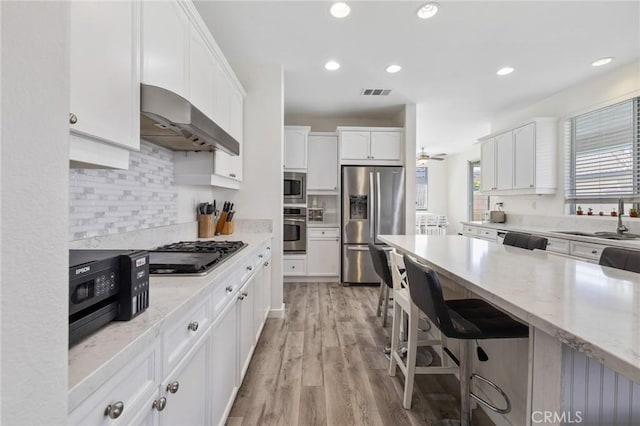 kitchen with appliances with stainless steel finishes, wall chimney range hood, a sink, white cabinetry, and light stone countertops