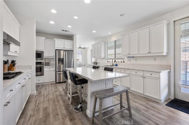 kitchen with appliances with stainless steel finishes, range hood, a kitchen bar, white cabinetry, and light wood-style floors
