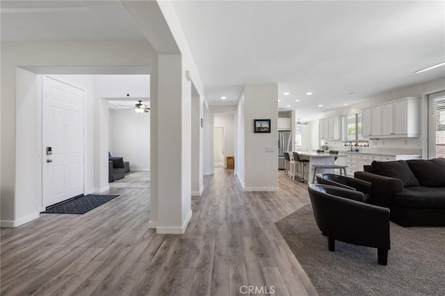 living area with light wood finished floors, a ceiling fan, baseboards, and recessed lighting