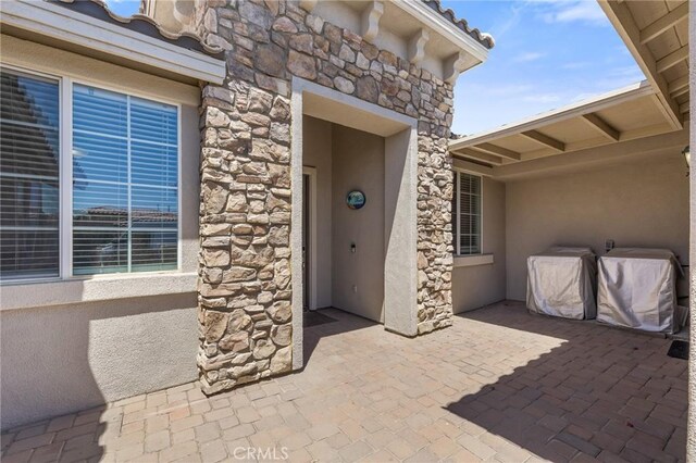 view of exterior entry with stone siding, a patio area, and stucco siding