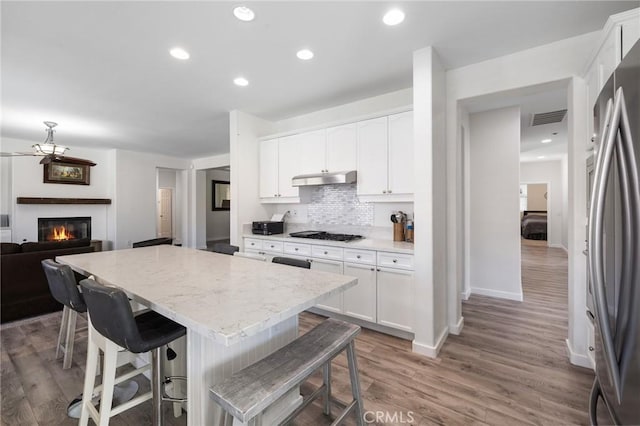 kitchen featuring freestanding refrigerator, under cabinet range hood, gas stovetop, a center island, and wood finished floors