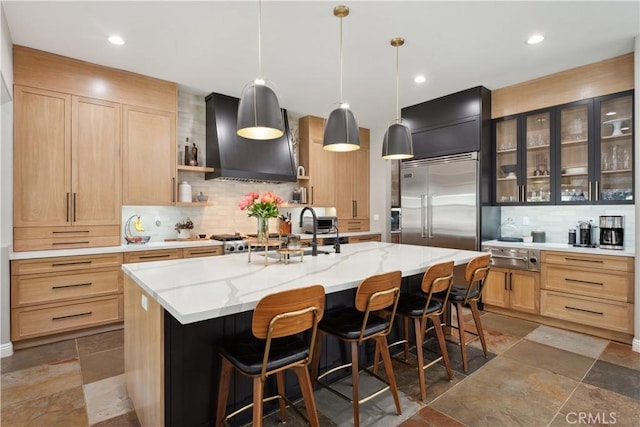 kitchen with wall chimney range hood, light brown cabinets, built in fridge, decorative backsplash, and open shelves