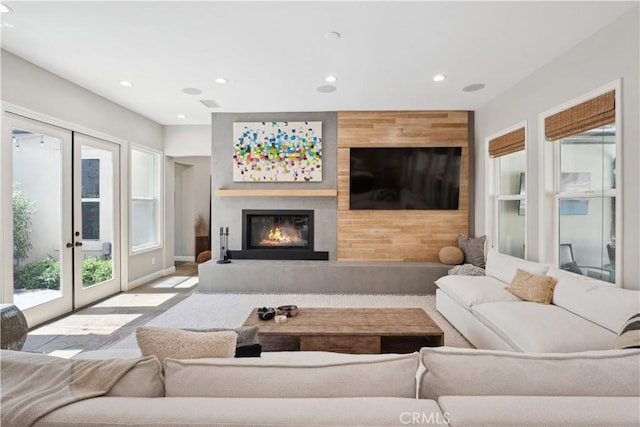 living room featuring a glass covered fireplace, recessed lighting, french doors, and baseboards