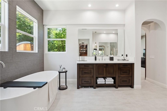 bathroom featuring vanity, a freestanding tub, tile patterned flooring, baseboards, and recessed lighting