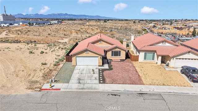 view of front of property featuring a tiled roof, concrete driveway, a mountain view, stucco siding, and view of desert landscape