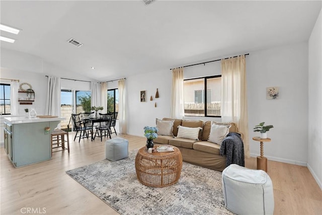living room with lofted ceiling, light wood-type flooring, and baseboards