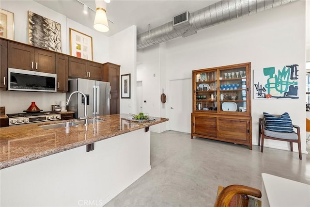 253 N Bush St, Santa Ana, CA 92701 - kitchen with appliances with stainless steel finishes, stone countertops, dark brown cabinetry, concrete flooring, and a high ceiling