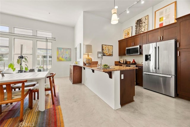 253 N Bush St, Santa Ana, CA 92701 - kitchen with stainless steel appliances, a peninsula, finished concrete flooring, rail lighting, and a high ceiling