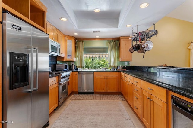 kitchen featuring high end appliances, recessed lighting, light tile patterned floors, a tray ceiling, and a sink