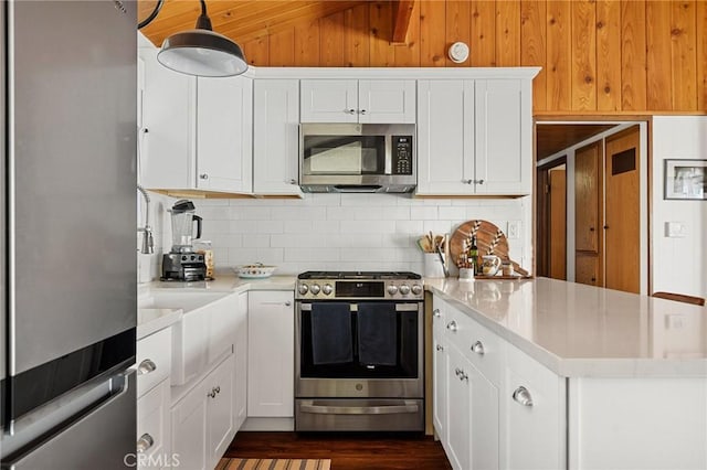 kitchen with stainless steel appliances, a peninsula, backsplash, light countertops, and white cabinets