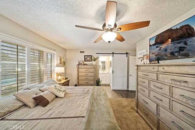1266 Marina Rd, Corona, CA 92880 - bedroom featuring a textured ceiling, a barn door, wood finished floors, connected bathroom, and ceiling fan