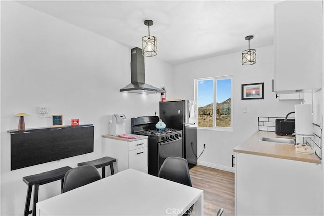 59101 Joshua Dr, Yucca Valley, CA 92284 - kitchen featuring wall chimney range hood, black gas stove, light countertops, light wood finished floors, and freestanding refrigerator