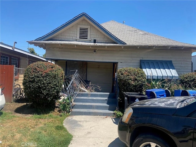view of front of property with covered porch, a shingled roof, and fence