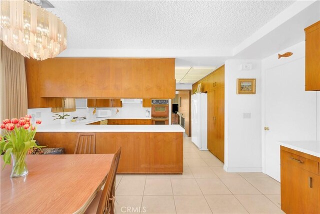 18132 James Rd, Villa Park, CA 92861 - kitchen featuring white appliances, a textured ceiling, light tile patterned floors, brown cabinets, and a peninsula