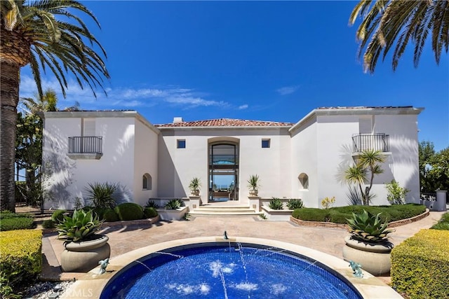rear view of property featuring stucco siding, a hot tub, a tile roof, and a balcony