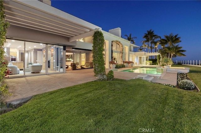 back of house at twilight with a patio area, a lawn, an outdoor pool, and a chimney