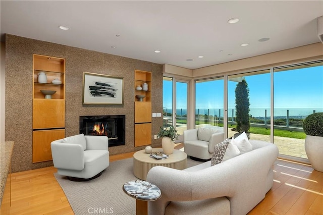 living room featuring wood finished floors, built in shelves, a fireplace, recessed lighting, and a water view
