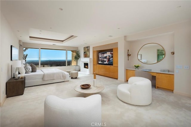 bedroom with a warm lit fireplace, a raised ceiling, light colored carpet, and baseboards