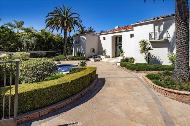 view of front of house featuring stucco siding, a tile roof, a balcony, and a chimney