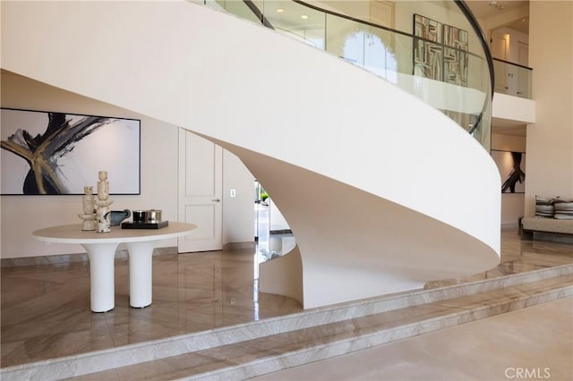 stairway featuring marble tiled flooring, baseboards, and a high ceiling