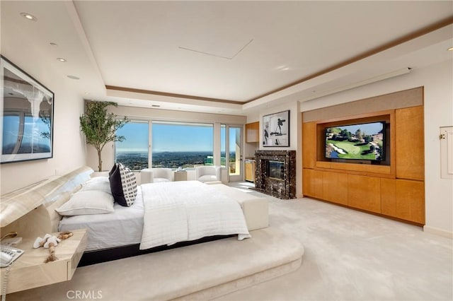 bedroom featuring a tray ceiling, light colored carpet, and a fireplace