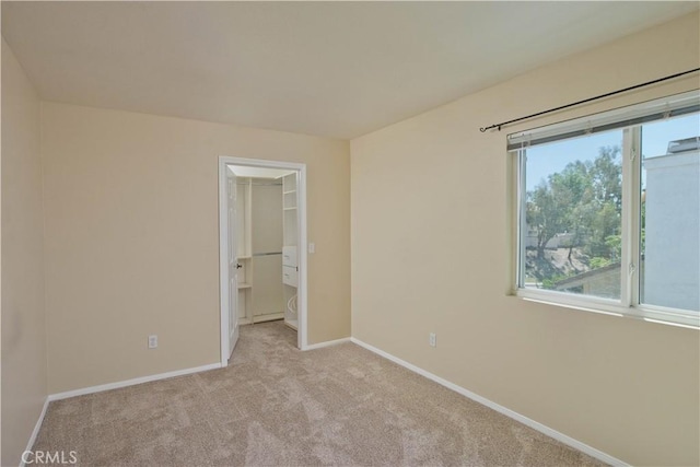 unfurnished bedroom with baseboards, light carpet, a spacious closet, and a closet