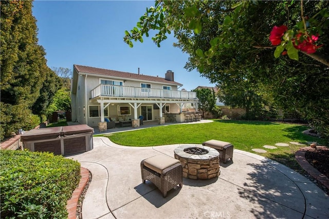 rear view of house with a hot tub, a patio, a chimney, a lawn, and an outdoor living space with a fire pit
