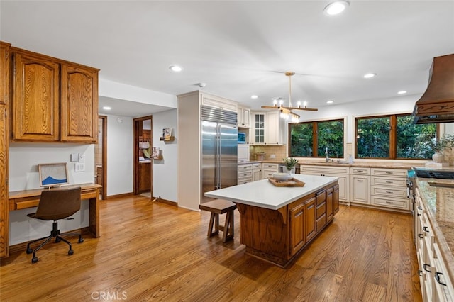 kitchen with stainless steel built in fridge, a sink, custom exhaust hood, light wood-style flooring, and light countertops