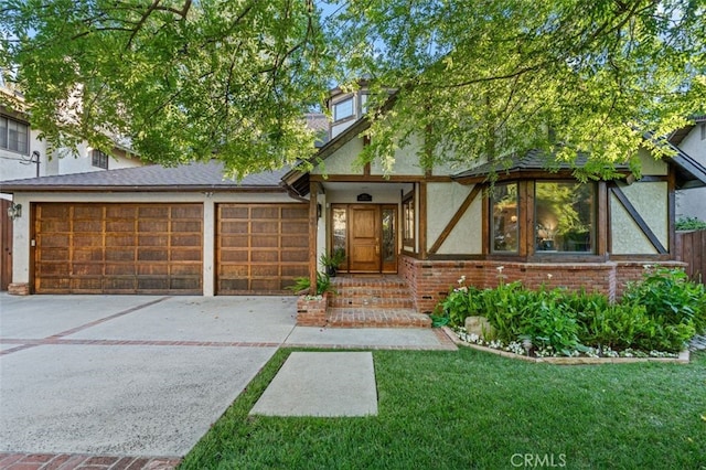 tudor house with a garage, stucco siding, concrete driveway, brick siding, and a front lawn