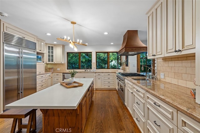 kitchen featuring high quality appliances, custom exhaust hood, cream cabinets, tasteful backsplash, and a sink